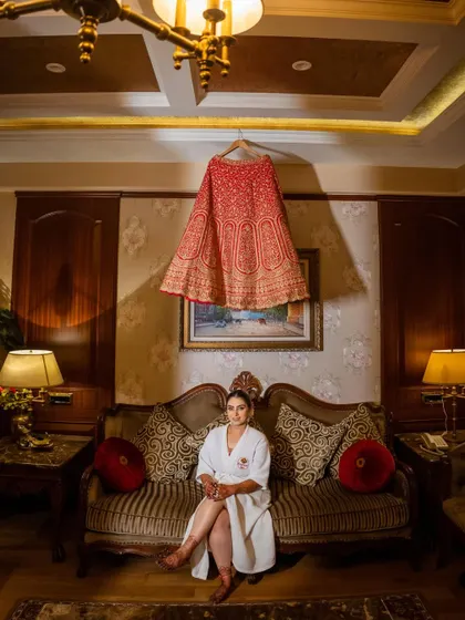 A relaxed portrait of the bride in her robe, sitting under her hanging wedding lehenga. A great "getting ready" shot.