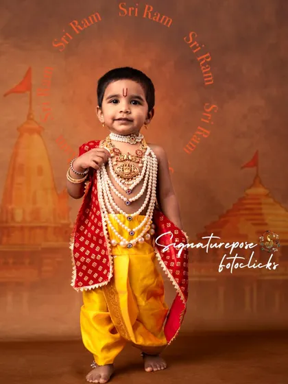 Dressed as the celebrated Ayodhya Baalarama, this little boy stands proudly. The portrait highlights the rich, detailed costume with layers of jewelry against a backdrop signifying the grand temple.
