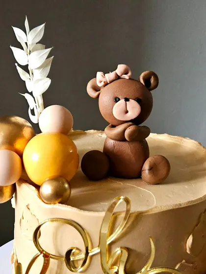 A close-up of the hand-sculpted teddy bear topper from the beige baby shower cake. The little bow adds a sweet, delicate touch.