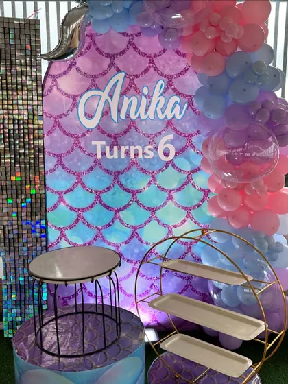 A personalized mermaid-themed backdrop for Anika's 6th birthday. The design features a shimmering scale pattern, the birthday girl's name, and a beautiful balloon garland in pastel pinks and blues.