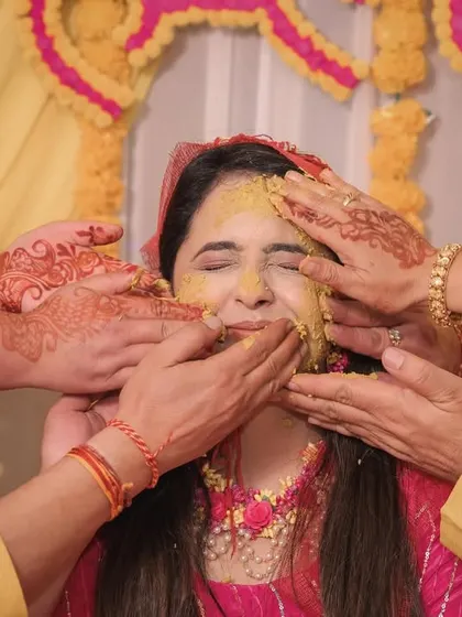 A close-up of the Haldi application, capturing the bride's expression of pure joy and the hands of her loved ones.