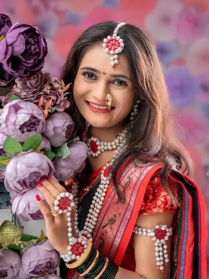 A beautiful individual portrait of a woman dressed for her Makarsankranti photoshoot. She is surrounded by purple flowers that complement her traditional red and black saree.