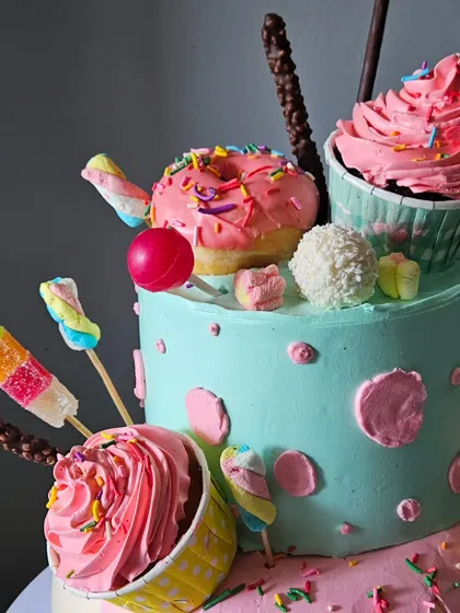 A close-up of the top tier of the whipped cream candyland cake, focusing on the detailed piping of the cupcakes and the placement of various candies.