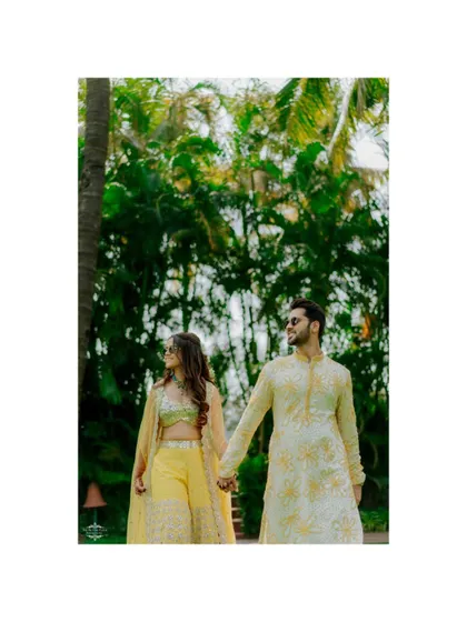 A stylish shot of the couple walking hand-in-hand, framed by lush greenery.