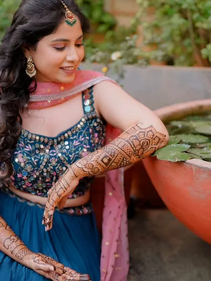 A relaxed pose by the lotus pond, showing the full extent of the mehndi on both her arms.