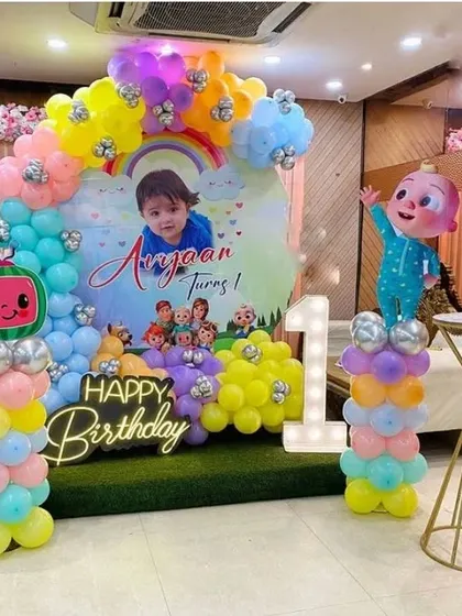 A Cocomelon first birthday setup with a personalized backdrop. The decoration features a pastel balloon arch and a marquee number '1'.