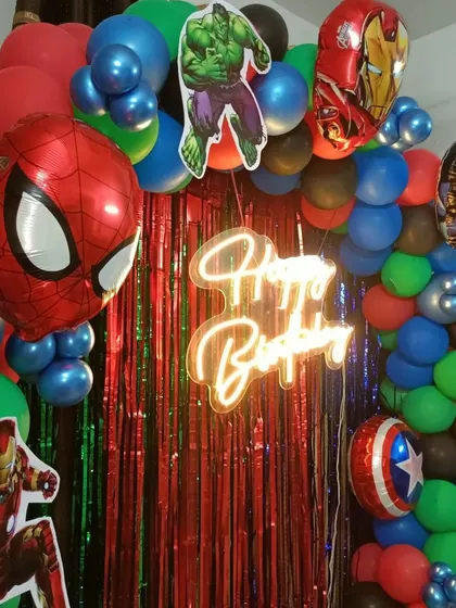 A close-up of the Avengers setup, highlighting the "Happy Birthday" neon sign against a red and green shimmer backdrop.