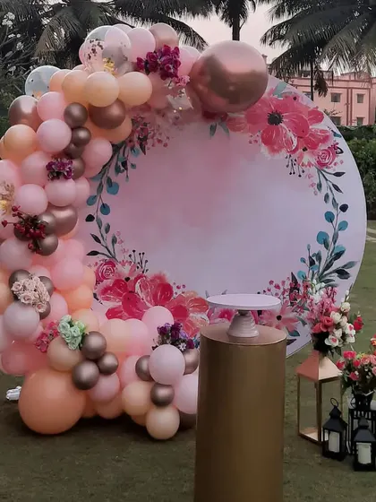 An elegant outdoor setup perfect for a mother's birthday or a bridal shower. It features a circular backdrop with a beautiful floral print, framed by a balloon arch in soft, romantic colors.