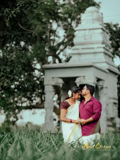 A tender moment with the groom kissing the bride's forehead, set against a backdrop of a field and a small temple.