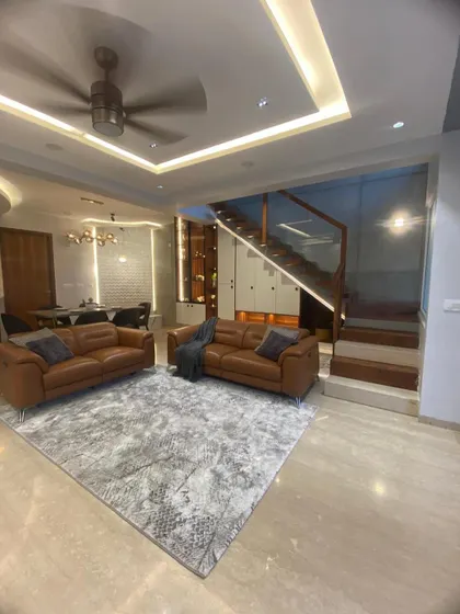 A full view of the living room, highlighting the plush leather sofas, modern rug, and the beautifully designed staircase in the background.