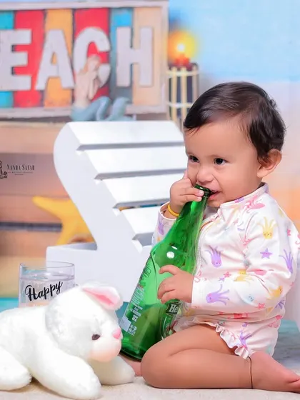 It's always fun to see what babies will do with the props. This moment of a baby chewing on a bottle prop is a perfect example of their cute and unpredictable nature.