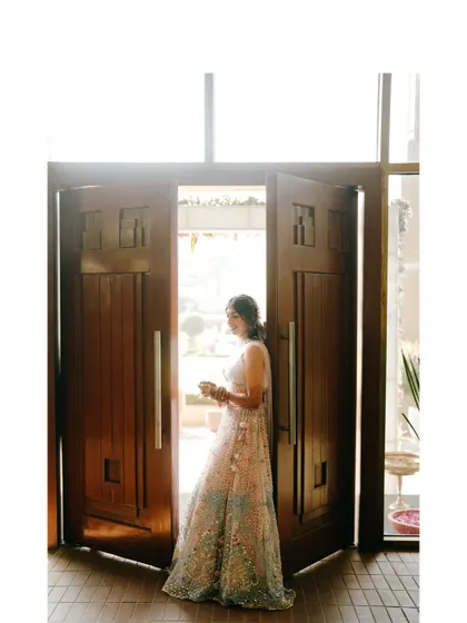 A grand entrance. The bride is framed by large wooden doors, creating a dramatic and beautiful portrait as she steps into her celebration.