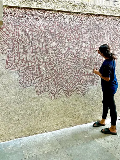 Painting a half mandala on a textured exterior wall for a cafe. The earthy brown tones blend beautifully with the outdoor setting.