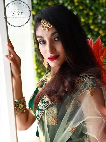 An editorial look that combines elegance and high fashion. The makeup is bold, with a sharp cat-eye and a classic red lip, paired with a modern green lehenga and statement jewellery.