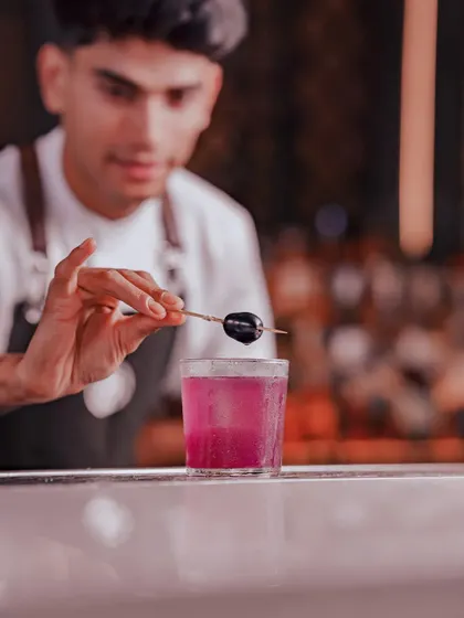 A bartender puts the finishing touch on the Jamun Twilight. This cocktail is a tropical escape, balancing the tangy sweetness of spiced jamun with fresh lime and our house gin. It’s a perfect drink for a good time.