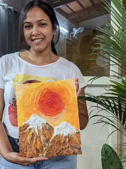 A participant with her vibrant texture painting of a sun setting over mountains. The texture adds a dramatic effect to the scene.