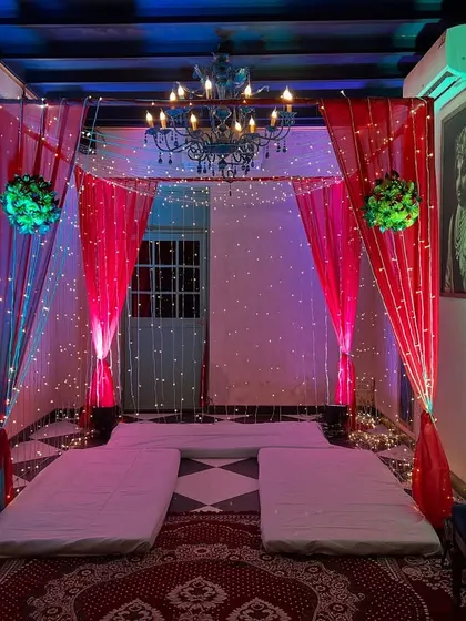 A cozy and traditional low-seating arrangement (baithak) with mattresses and bolsters, decorated with a canopy of drapes, fairy lights, and a chandelier.