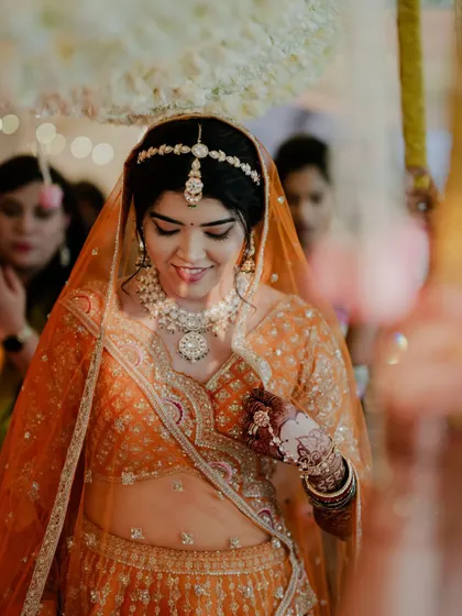 Reeya walked down the aisle for her beautiful sunset Varmala in this gorgeous orange lehenga. We paired it with a fresh matte face, copper-hued eyes, and blooms in her bun that matched her outfit, creating a stunning Marwadi bridal look.