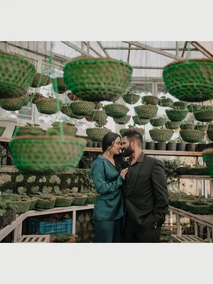 An intimate portrait of a couple surrounded by hanging planters in a Mussoorie nursery. The unique framing and soft focus create a sense of privacy and romance.