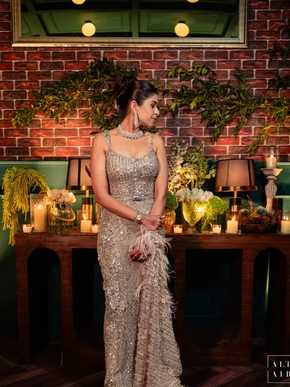 The beautiful bride at her glass house reception. The backdrop of exposed brick and a vintage console table styled with candles and lamps reflects the "old meets new" theme of the evening.