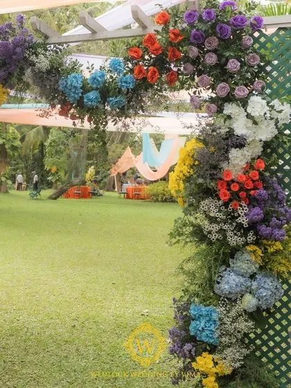 A vibrant floral backdrop and welcome sign for a colorful Haldi and Mehendi ceremony. The mix of orange, blue, purple, and yellow flowers created a stunning photo opportunity for the couple and their guests.