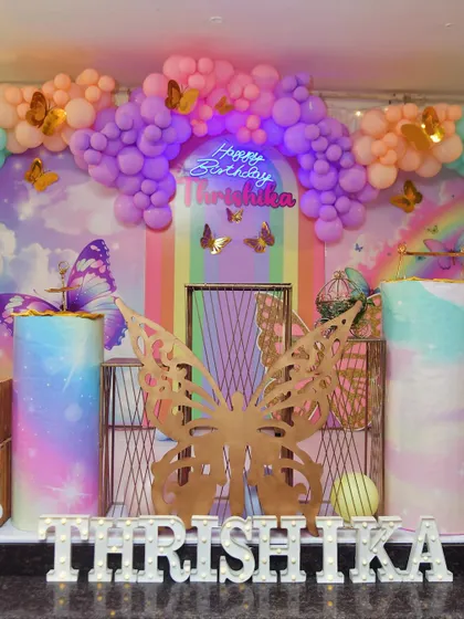 A closer view of the pastel rainbow butterfly setup, highlighting the neon 'Happy Birthday' sign and themed cake tables.
