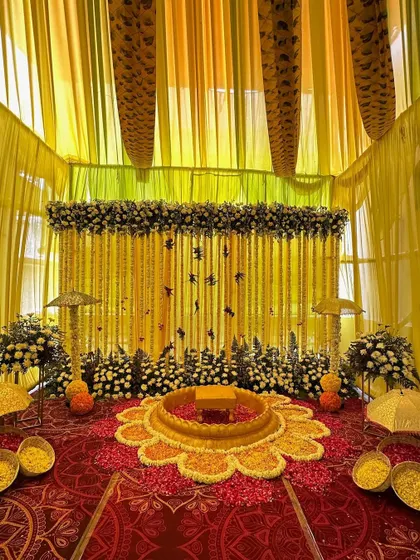 An intimate and traditional Haldi seating area. We created a flower-shaped arrangement on the floor with marigold petals and a backdrop of hanging floral strings and decorative umbrellas.