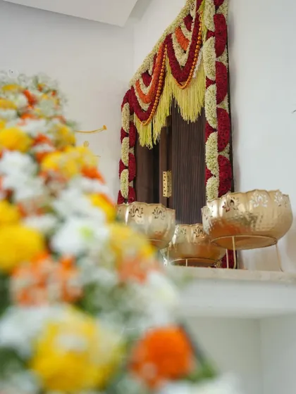 A close-up of the traditional floral decor at the entrance of a home for a Grah Pravesh ceremony. The blurred foreground of marigolds draws attention to the beautifully decorated doorway.
