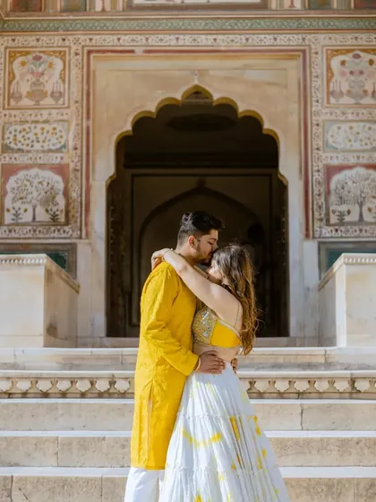 A romantic embrace in front of the detailed facade of a Jaipur palace. The groom's bright yellow kurta and the bride's coordinated lehenga bring a joyful energy to this royal pre-wedding photo.