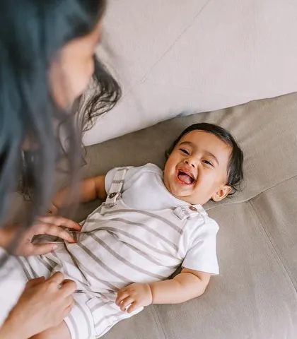 A mother tickling her laughing baby on the sofa. The beautiful natural light and their genuine happiness make this a perfect lifestyle shot.
