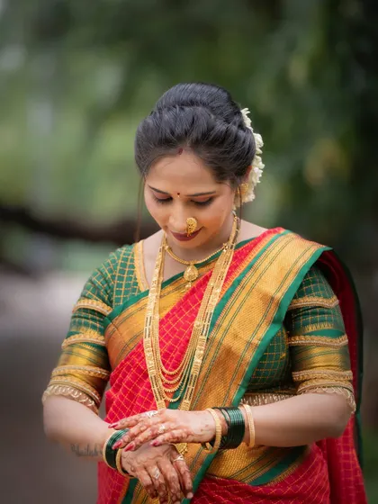 A close-up shot focusing on the details of the Vat Purnima preparations. The woman, dressed in a traditional red and green saree, looks at her hands adorned with henna, ready for the puja.