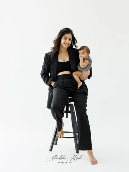 A modern and powerful portrait of motherhood. A mother dressed in a stylish black suit holds her baby, blending strength and tenderness beautifully.