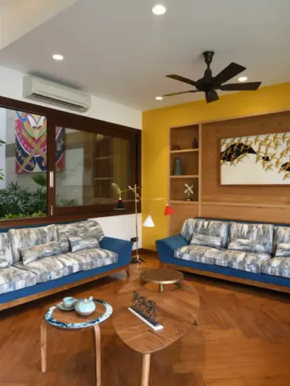 The drawing room at Ashraya Residence connects to both the internal courtyard and the garden through large sliding glass panels. These openings frame picturesque views and facilitate natural cross-ventilation, blurring the lines between indoors and outdoors.
