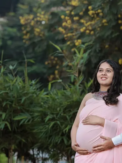 An expecting couple looking towards the future, surrounded by the lush greenery of a park.