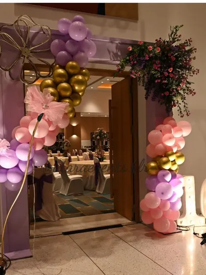 A balloon and floral archway at the entrance to an Aqeeqah celebration. The pink, purple, and gold colors create a grand and festive welcome for guests.