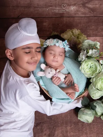 A big brother gently holds his baby sister, who is nestled in a basket of flowers. The look of adoration on his face is just priceless.