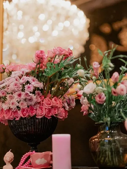 A close-up of a decorative vignette, with pink floral arrangements set before a gilded mirror. The reflection of the chandelier adds another layer of sparkle and luxury.