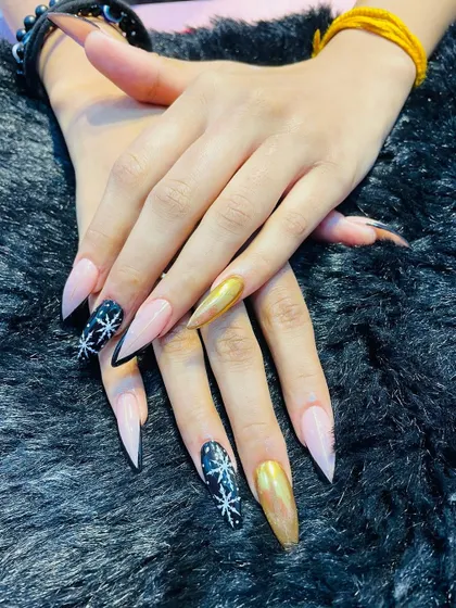 A dramatic and glamorous winter look. These long stiletto nails combine a striking gold chrome, a deep black with hand-painted snowflakes, and a soft nude base for a high-contrast, statement-making set.