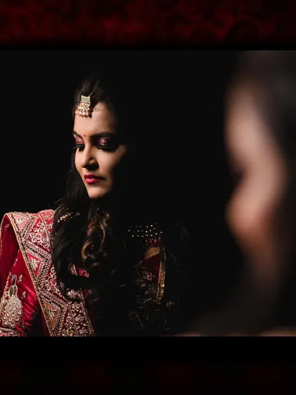 A beautiful, moody portrait of the bride at her reception. The dark background and soft lighting highlight her features and elegant red lehenga.