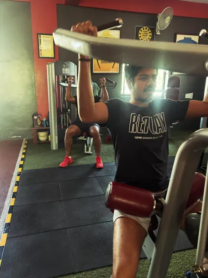 A client works his back on a pulldown machine while another trains in the background, showing the focused energy of our gym.