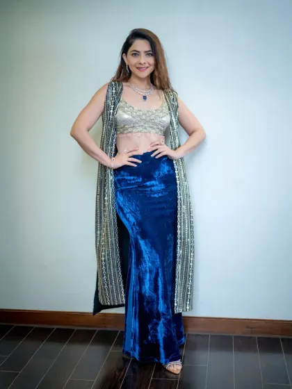 A full-length studio portrait against a clean white background. This allows the model's vibrant blue and gold outfit to be the main focus of the image.