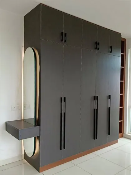 A modern grey wardrobe with a built-in dressing table and an elegantly backlit oval mirror.
