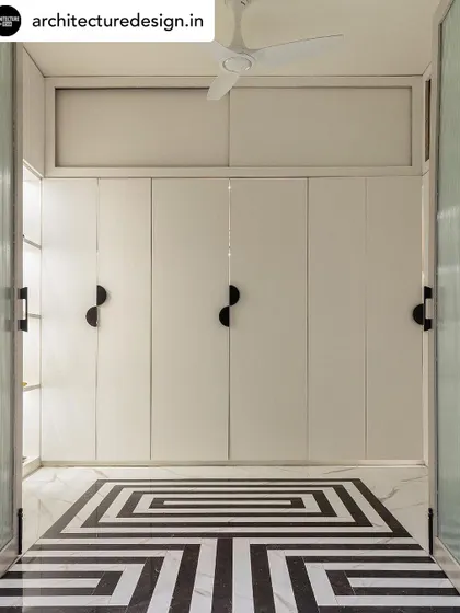 A walk-in closet with a bold, geometric-patterned marble floor. The clean lines of the white wardrobes and the unique black handles create a modern and organized space.