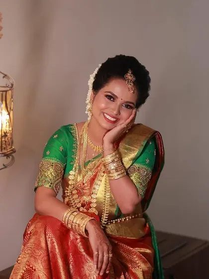 A joyful portrait of bride Jaswitha. The warm lighting highlights her glowing skin and the rich colors of her green and red bridal saree.