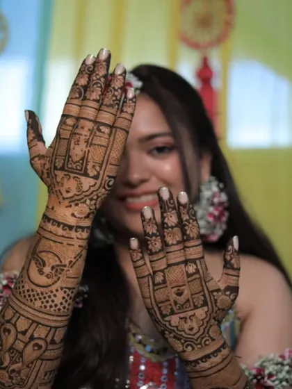 A playful bride peeking through her hands, which are covered in a beautiful back-hand mehandi design.