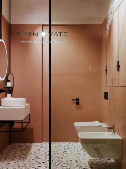 A bold bathroom design featuring monochromatic pink walls and terrazzo flooring. The wall-mounted toilet and floating sink add to the minimalist aesthetic.