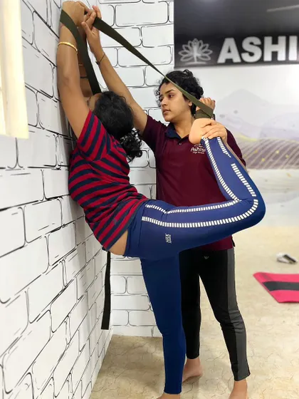 Wall ropes and straps are excellent tools for deep stretching. An instructor assists a student in a standing backbend, targeting shoulder and spine flexibility.