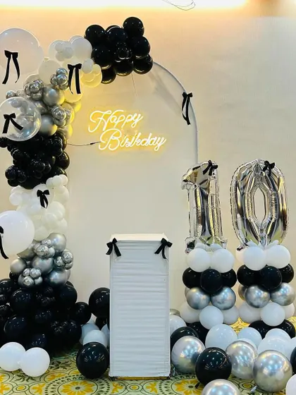 A full view of the chic black and white bow-themed 10th birthday. The asymmetrical balloon arch and number columns create a modern look.