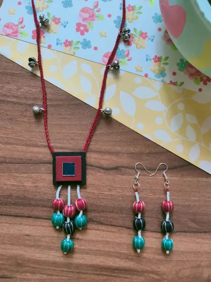 This necklace set features a fabric pendant with colorful thread-wrapped beads. The matching long earrings complete the look, making it an easy choice for Durga Puja or Navratri celebrations.