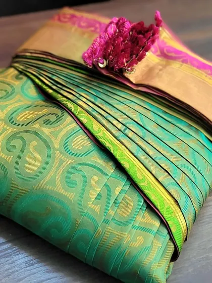 A client's green Kanjivaram saree with a bright pink pallu, perfectly folded.